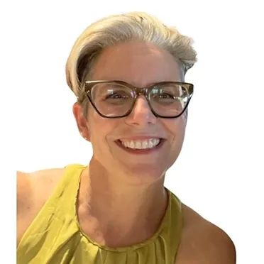 Smiling woman with short blonde hair wearing large tortoiseshell glasses and a yellow sleeveless top.