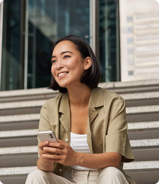 Smiling woman with short hair sitting on outdoor steps holding a smartphone.
