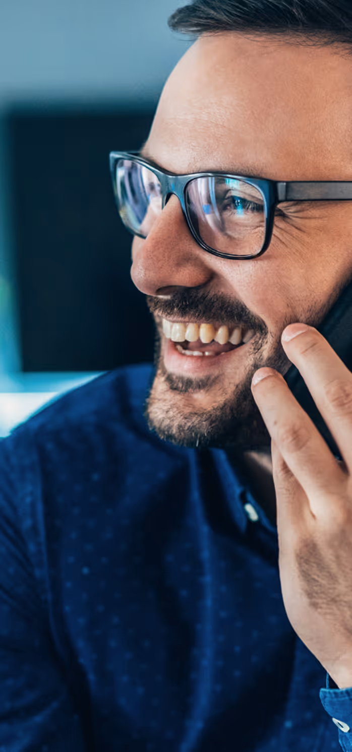 Homme souriant portant des lunettes et une chemise bleue, parlant au téléphone.