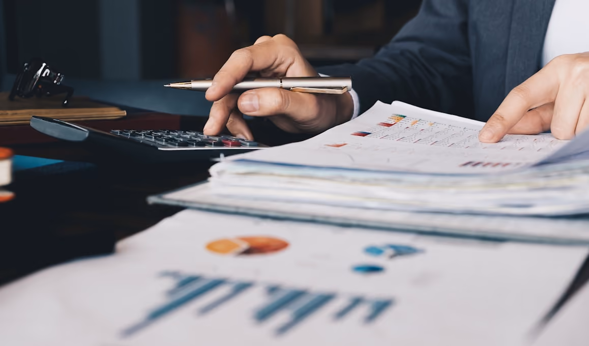 Une personne en costume utilise une calculatrice et examine des documents financiers avec des graphiques.