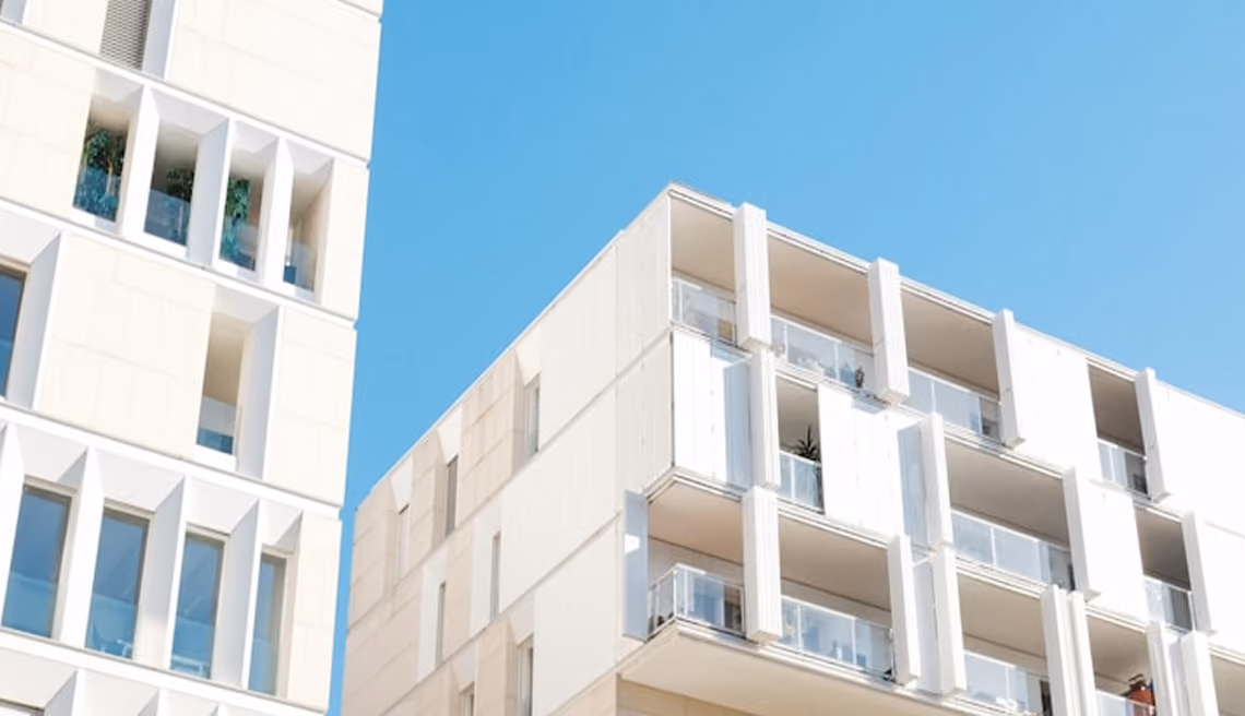 Façades modernes d'immeubles résidentiels blancs avec balcons en verre sous un ciel bleu clair.
