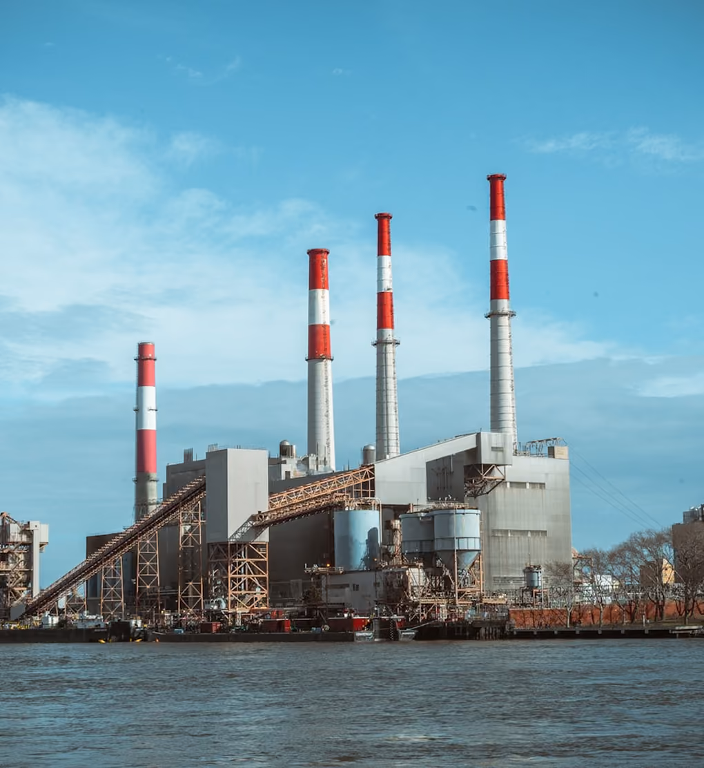 Usine avec quatre grandes cheminées rouges et blanches au bord d'une étendue d'eau.