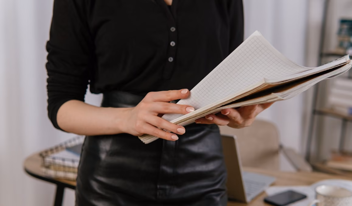 Personne tenant un cahier à feuilles quadrillées debout dans un bureau avec un bureau en arrière-plan.