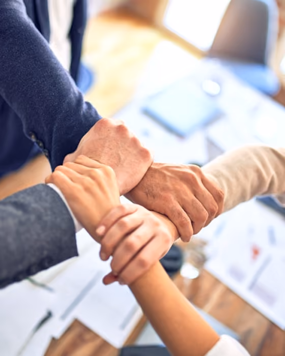 Quatre mains d'adultes réunies en pile, symbolisant le travail d'équipe au bureau.