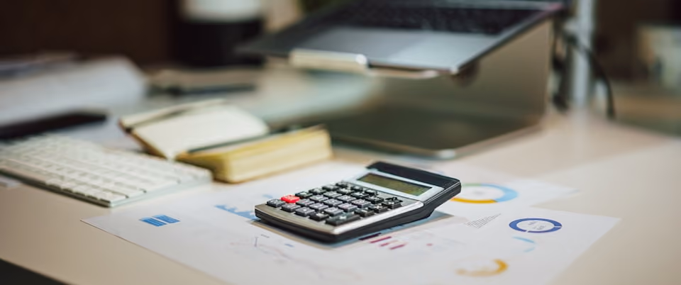 Une calculatrice sur des documents avec graphiques et un clavier et ordinateur en arrière-plan.