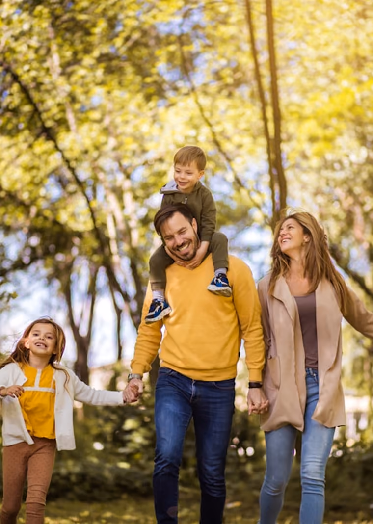 Famille marchant ensemble dans un parc avec un garçon sur les épaules du père et mère tenant leurs mains.