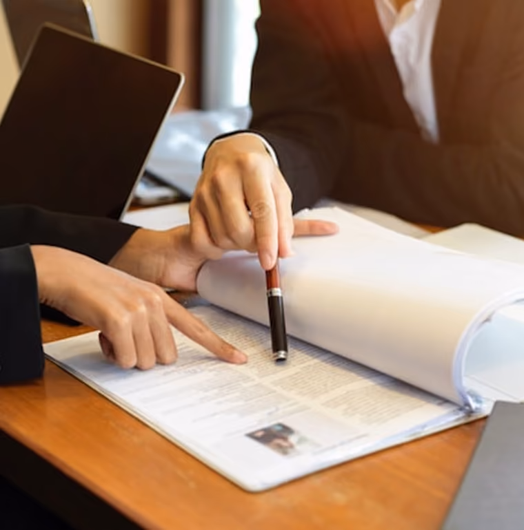 Deux personnes en costume discutent d'un document, l'une pointe le texte, l'autre avec un stylo.