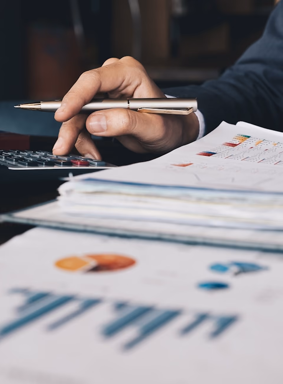 Main tenant un stylo et utilisant une calculatrice sur un bureau avec des documents imprimés.