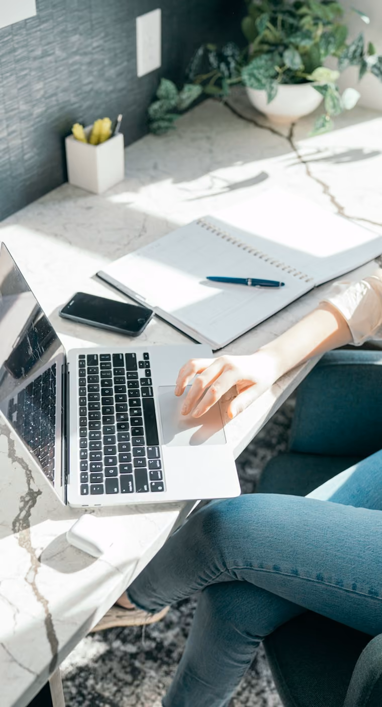 Une personne utilise un ordinateur portable sur un bureau en marbre avec un carnet et un téléphone.