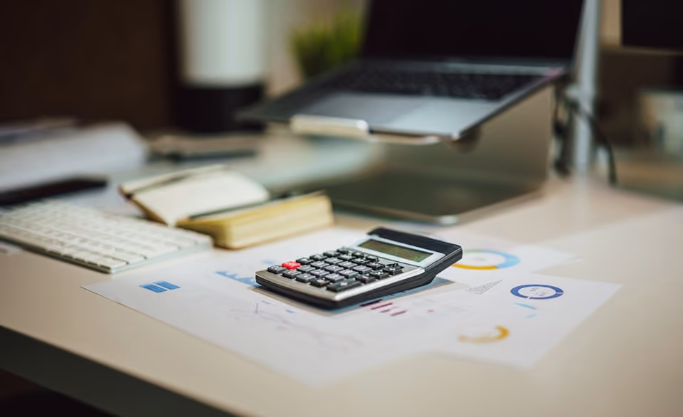 Calculatrice posée sur des feuilles avec graphiques à côté d'un clavier et d'un ordinateur portable.