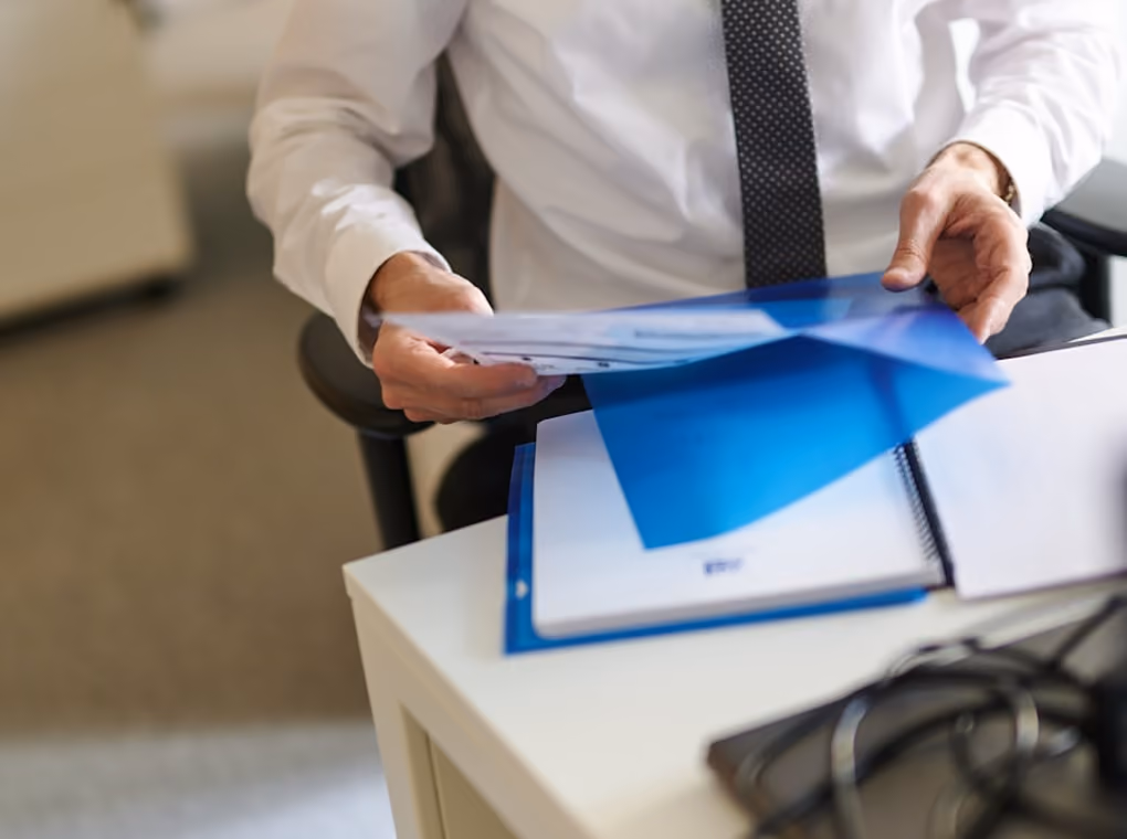Une personne en chemise blanche et cravate noire manipulant des documents sur un bureau blanc.