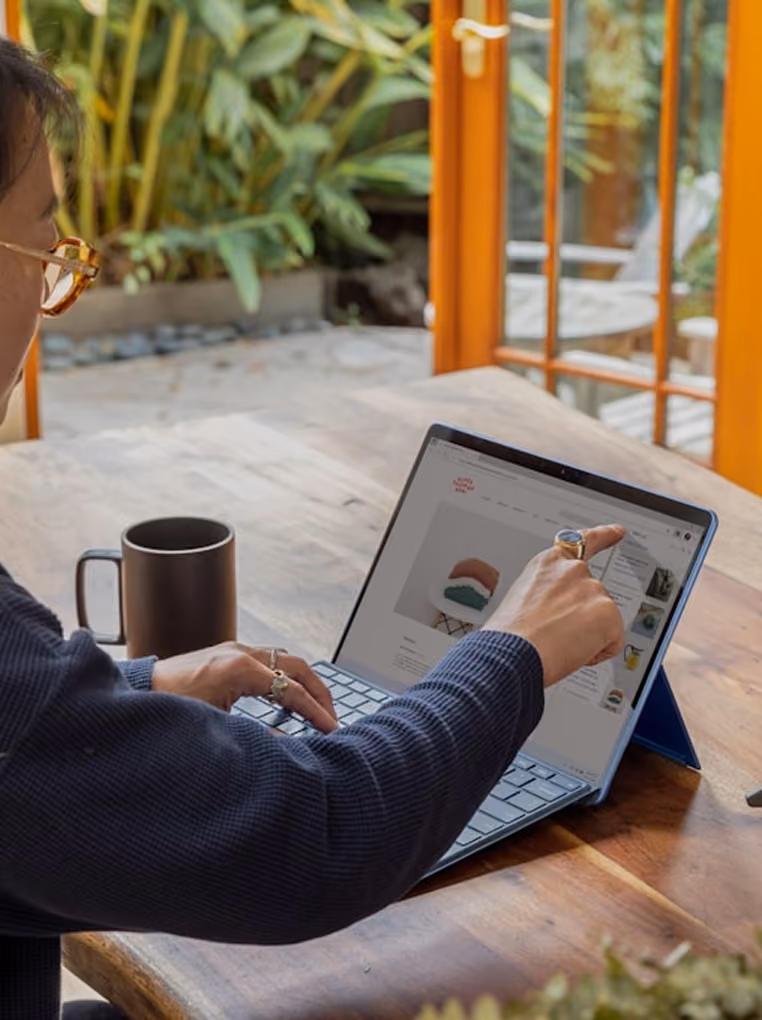 Personne utilisant une tablette avec clavier, montrant un site web, avec une tasse sur la table en bois.