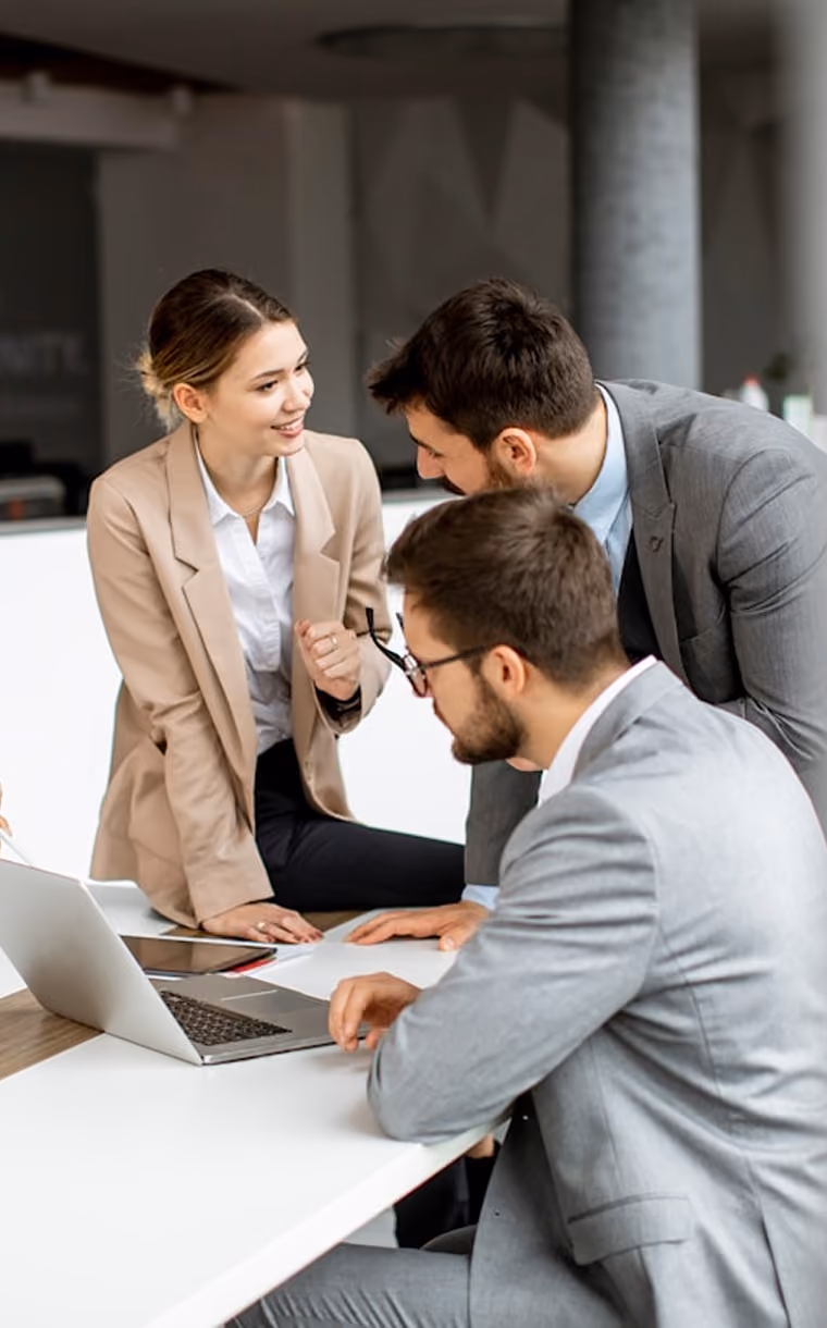 Trois professionnels en costumes discutent autour d'un ordinateur portable dans un bureau moderne.