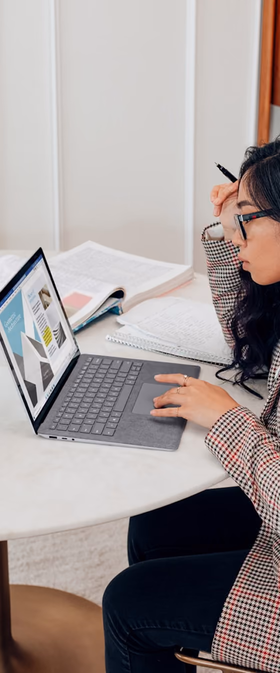 Une femme concentrée travaillant sur un ordinateur portable avec des notes et des livres sur la table.