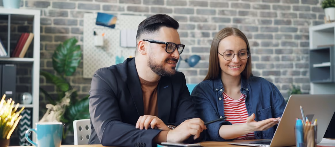 Un homme et une femme souriants travaillant ensemble sur un ordinateur portable dans un bureau.