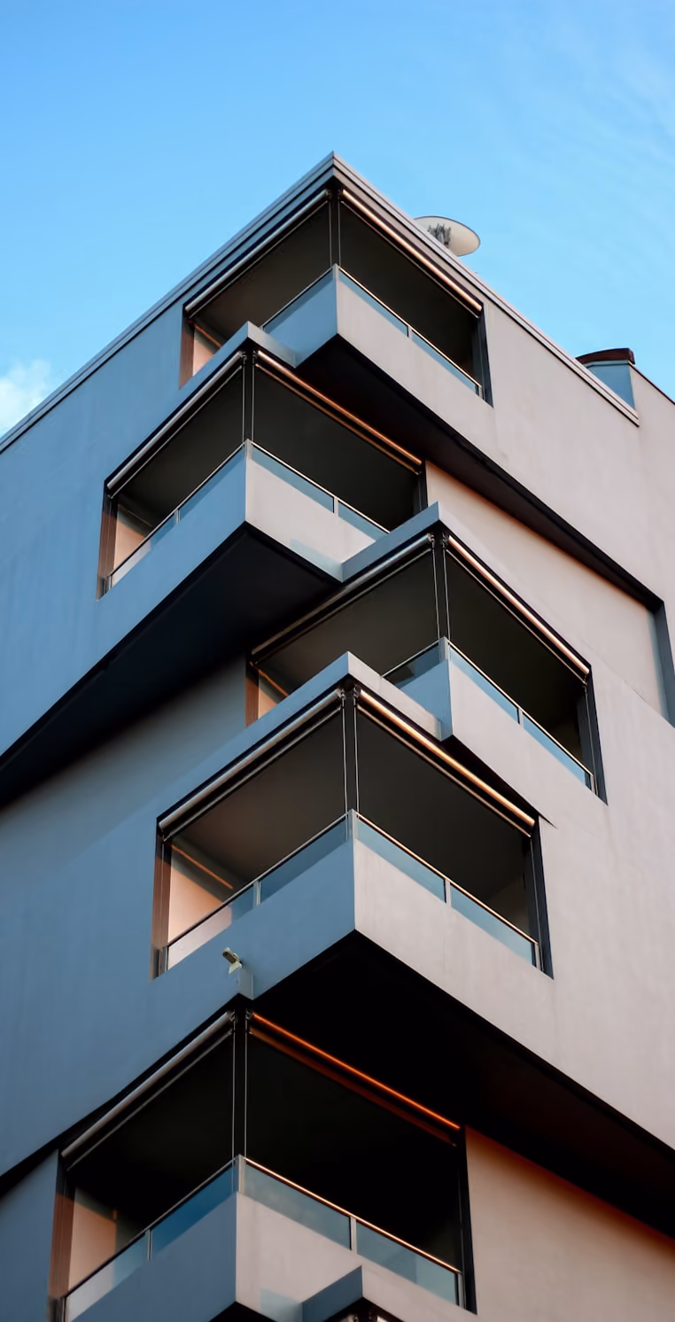 Façade d'immeuble moderne avec plusieurs balcons en angle sous un ciel bleu clair.