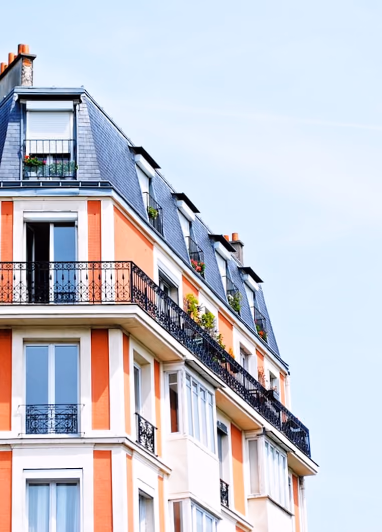Façade d'un immeuble parisien avec balcons en fer forgé et toit mansardé sous un ciel clair.