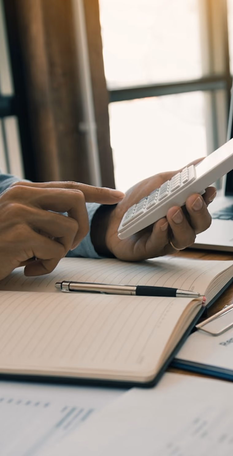 Une personne utilise une calculatrice blanche près d'un cahier ouvert avec un stylo posé dessus.
