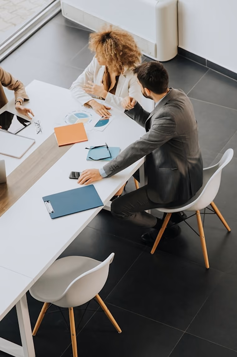 Deux professionnels discutant autour d'une table blanche avec des documents et des appareils électroniques.