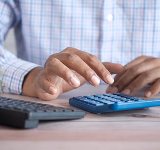 Une personne utilise une calculatrice bleue posée sur une table en bois.