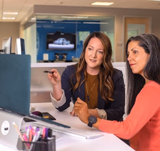 Deux femmes discutent devant un ordinateur dans un bureau moderne.