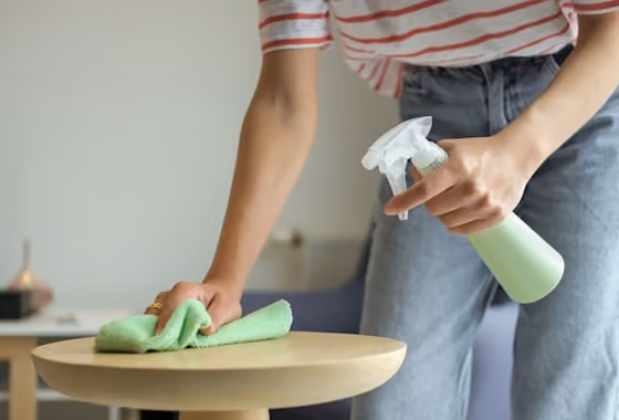 Personne nettoyant une table ronde en bois avec un chiffon vert et un spray de nettoyage