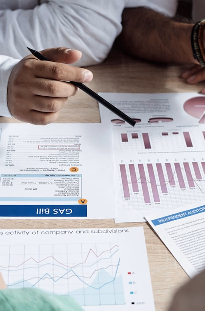 Main tenant pointant un graphique avec un stylo lors d'une réunion d'affaires autour de documents financiers.