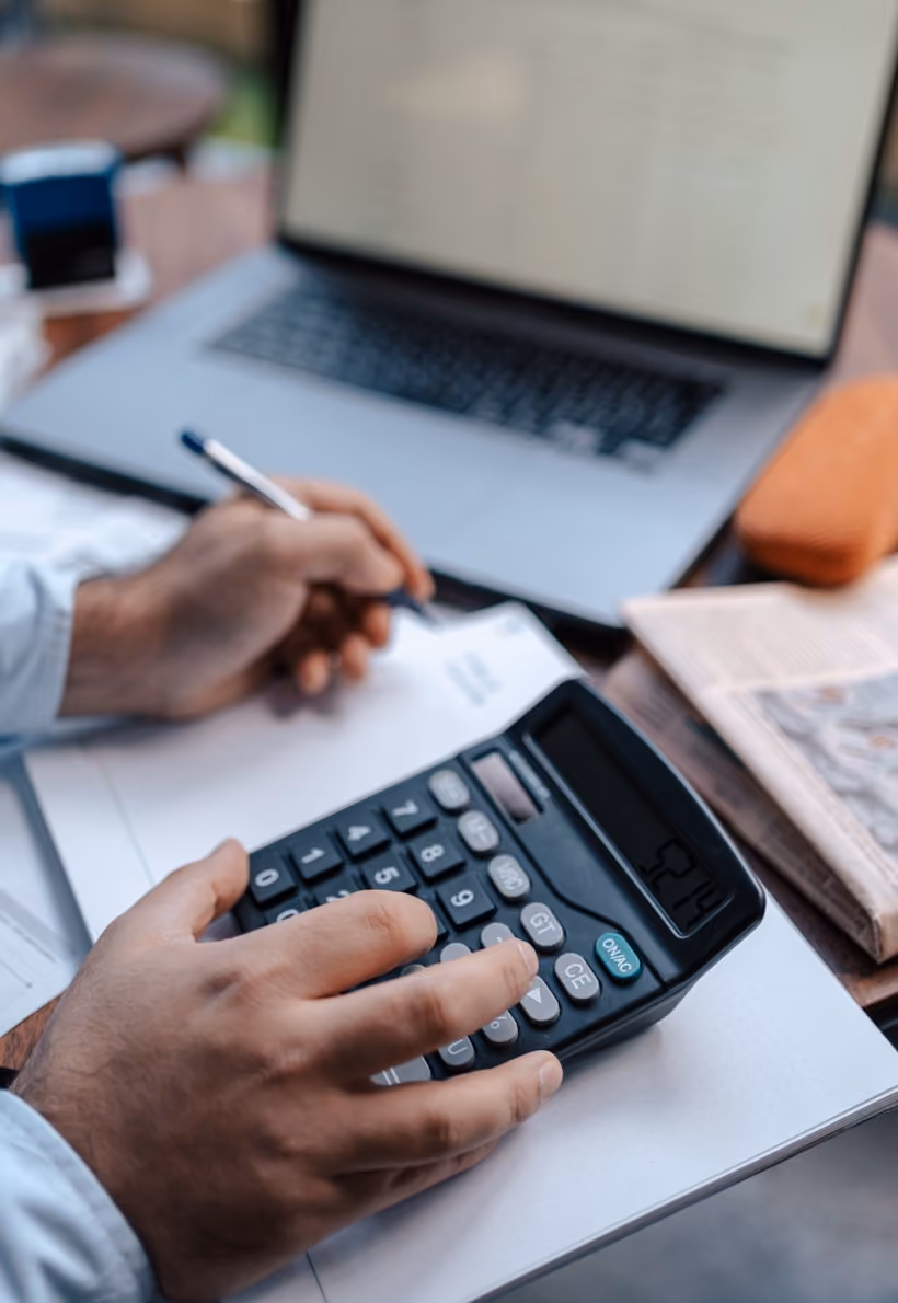 Une personne utilisant une calculatrice et écrivant sur un carnet devant un ordinateur portable.