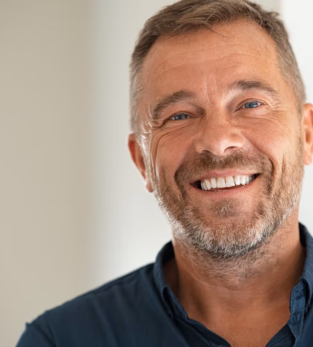 Homme souriant avec barbe, cheveux courts, portant une chemise bleue foncée.
