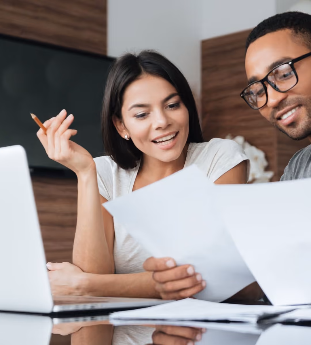 Deux collègues souriants examinent des documents ensemble devant un ordinateur portable.