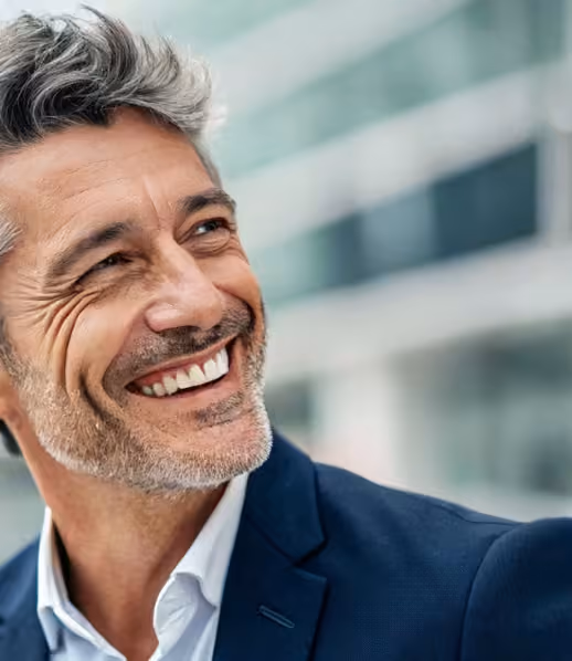 Homme souriant avec cheveux grisonnants et veste bleue devant un bâtiment moderne.