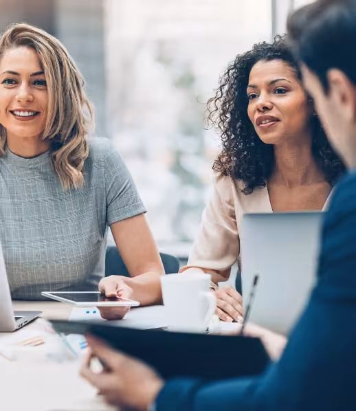 Trois professionnels en réunion, deux femmes souriantes et un homme consultant un document.