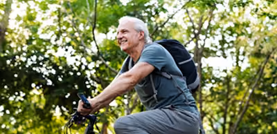 Un homme souriant fait du vélo dans un parc avec des arbres verts en arrière-plan.