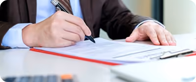 Une personne en costume signe un document sur un bureau avec un stylo noir.