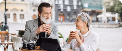 Un homme et une femme âgés sourient en buvant du café en terrasse d'un café.
