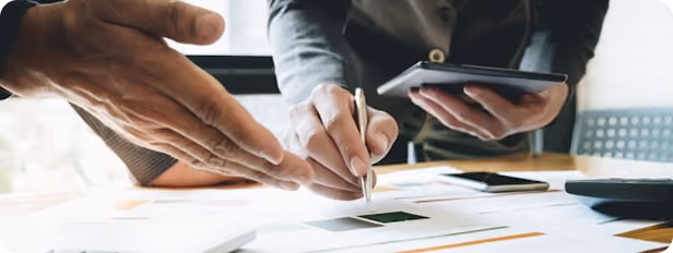 Deux personnes discutent et examinent des documents avec un stylo et une tablette sur une table.