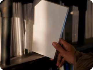 Une main saisit un livre à couverture blanche sur une étagère sombre remplie de livres.