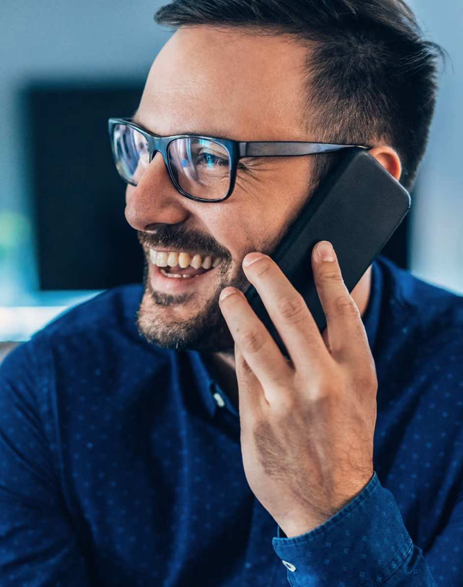 Homme souriant portant des lunettes parlant au téléphone portable noir.