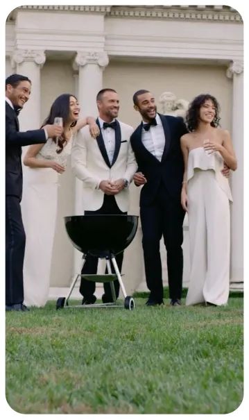 People dressed formally chatting and grilling outdoors.