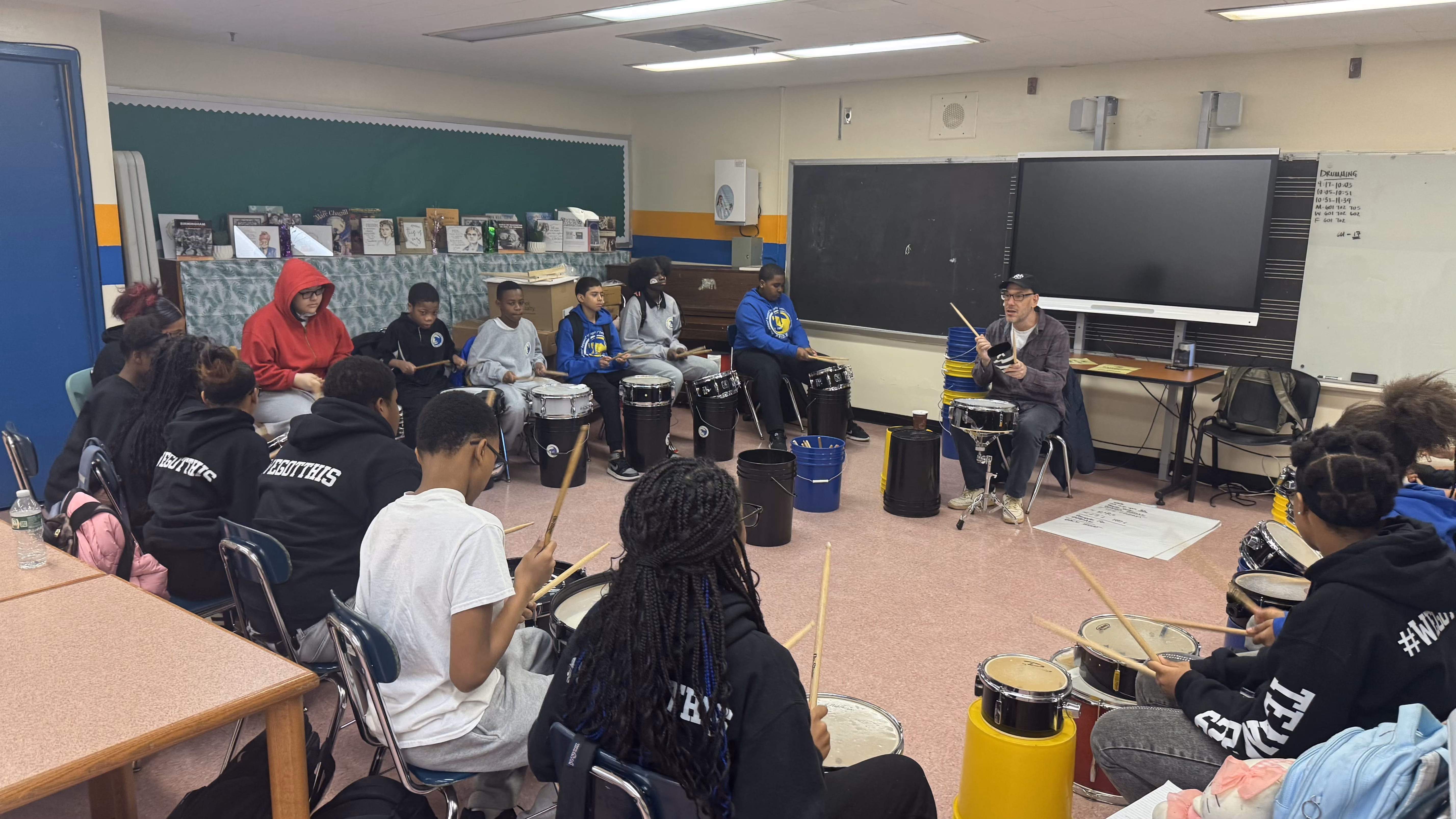 Students learning drumming with an instructor in a classroom