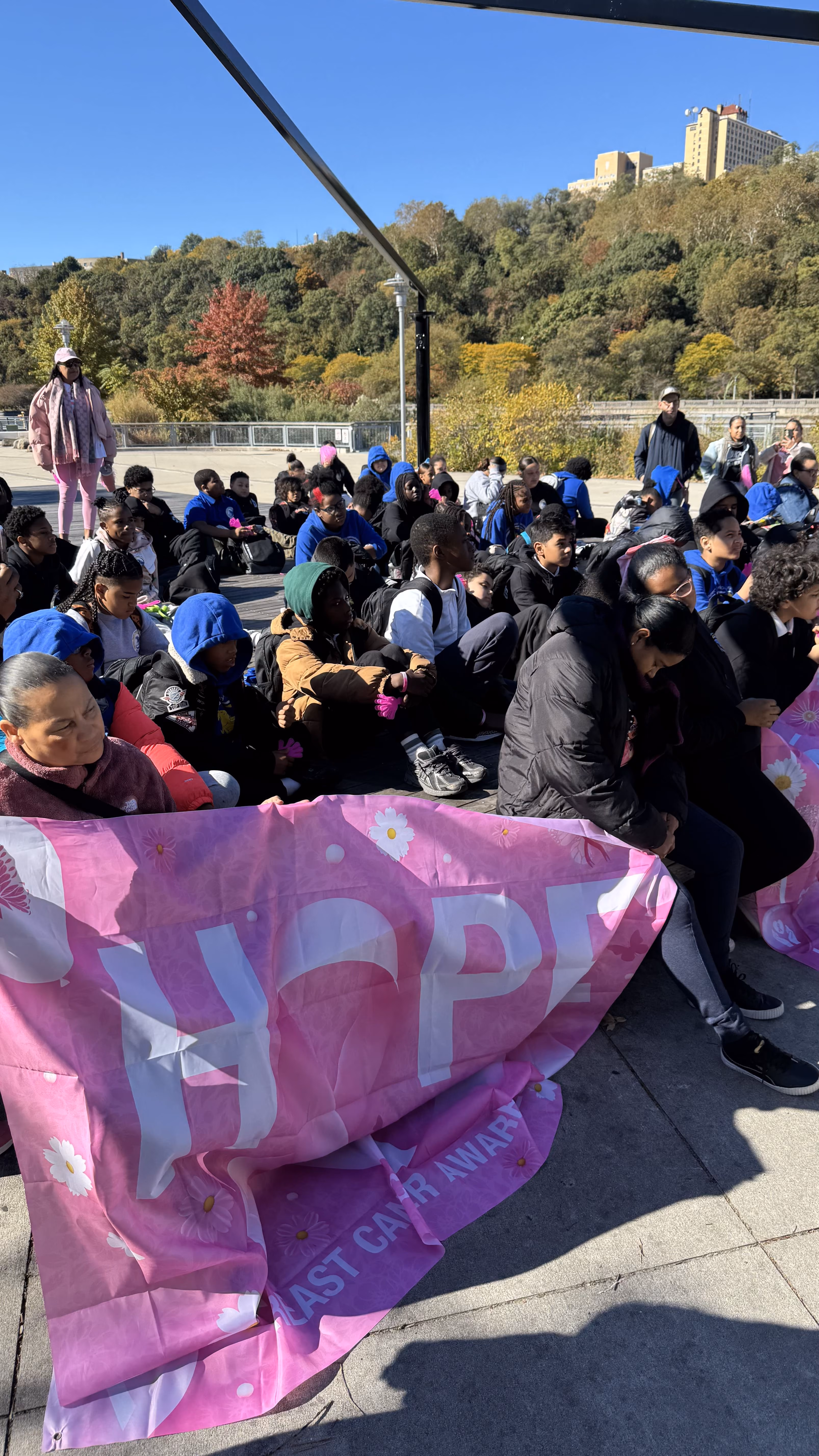 Students seated outdoors at breast cancer awareness walk holding Hope banner