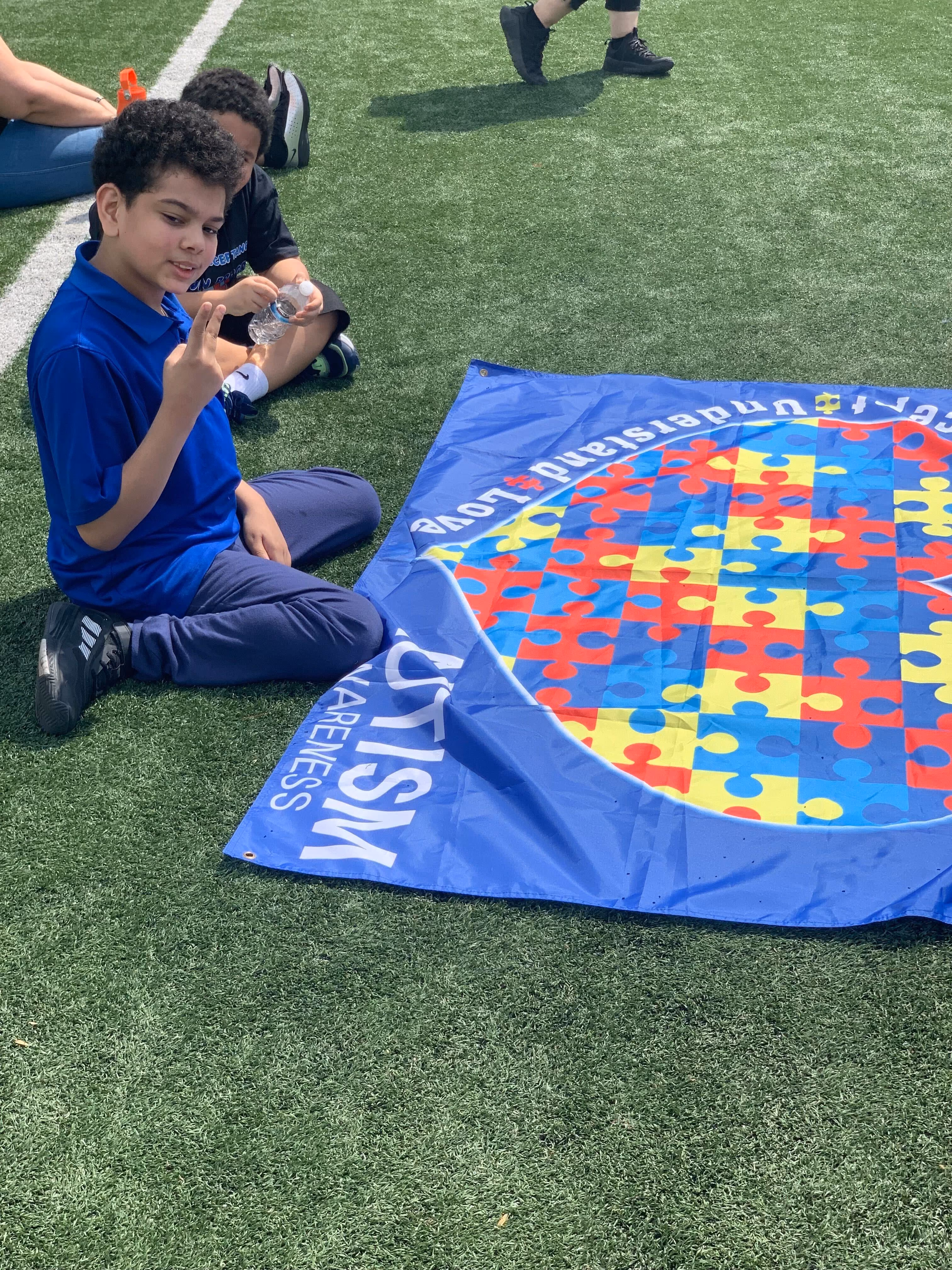 Student sitting on field beside autism awareness banner at outdoor event