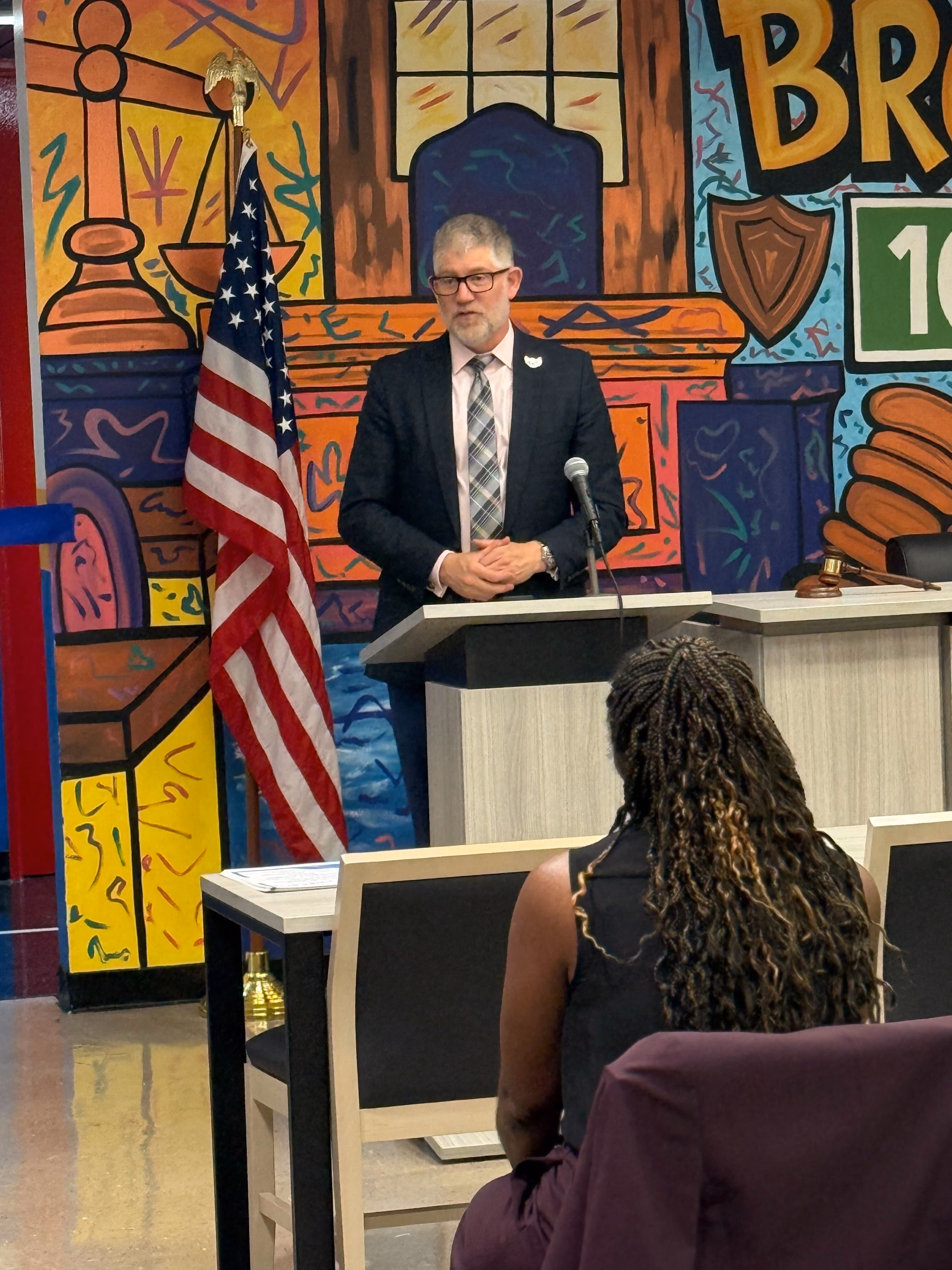 Man in suit speaking at podium during school board meeting