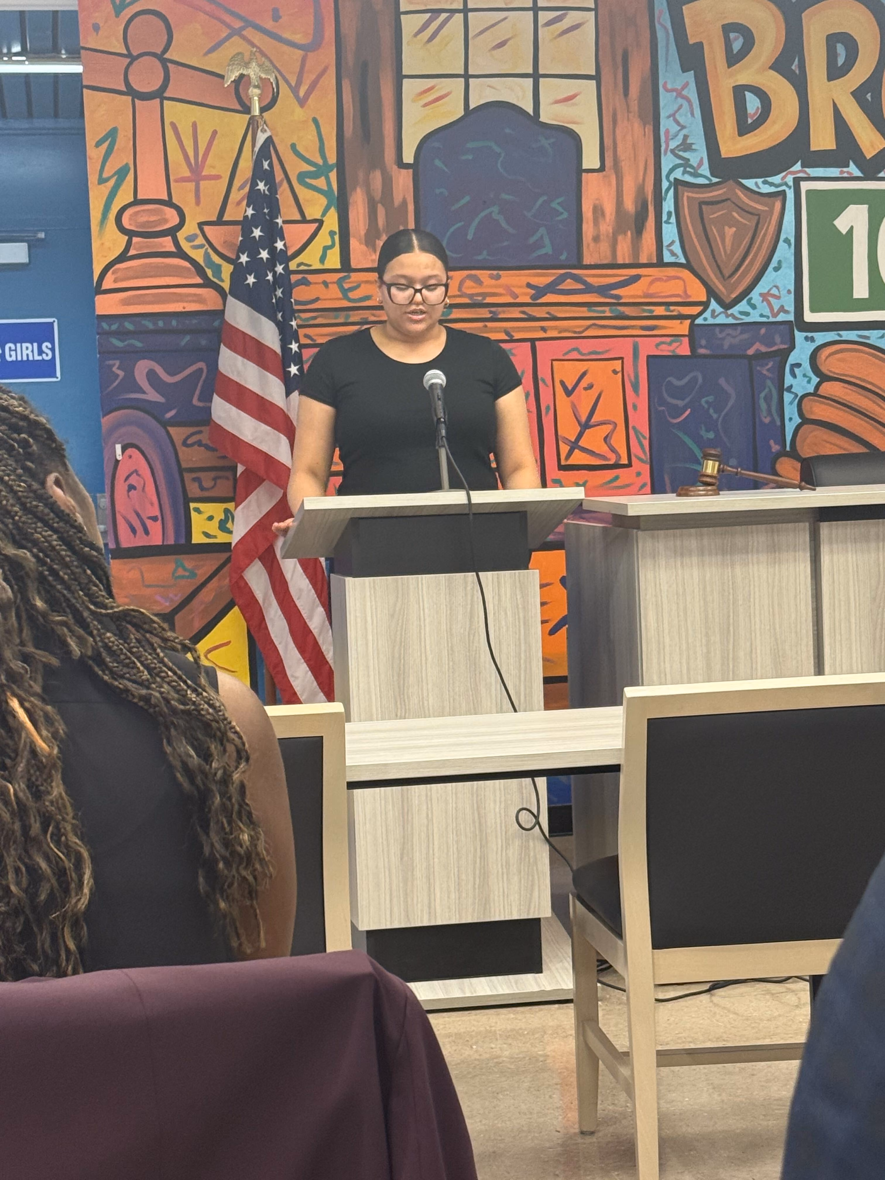 Student speaks at podium during school event with American flag