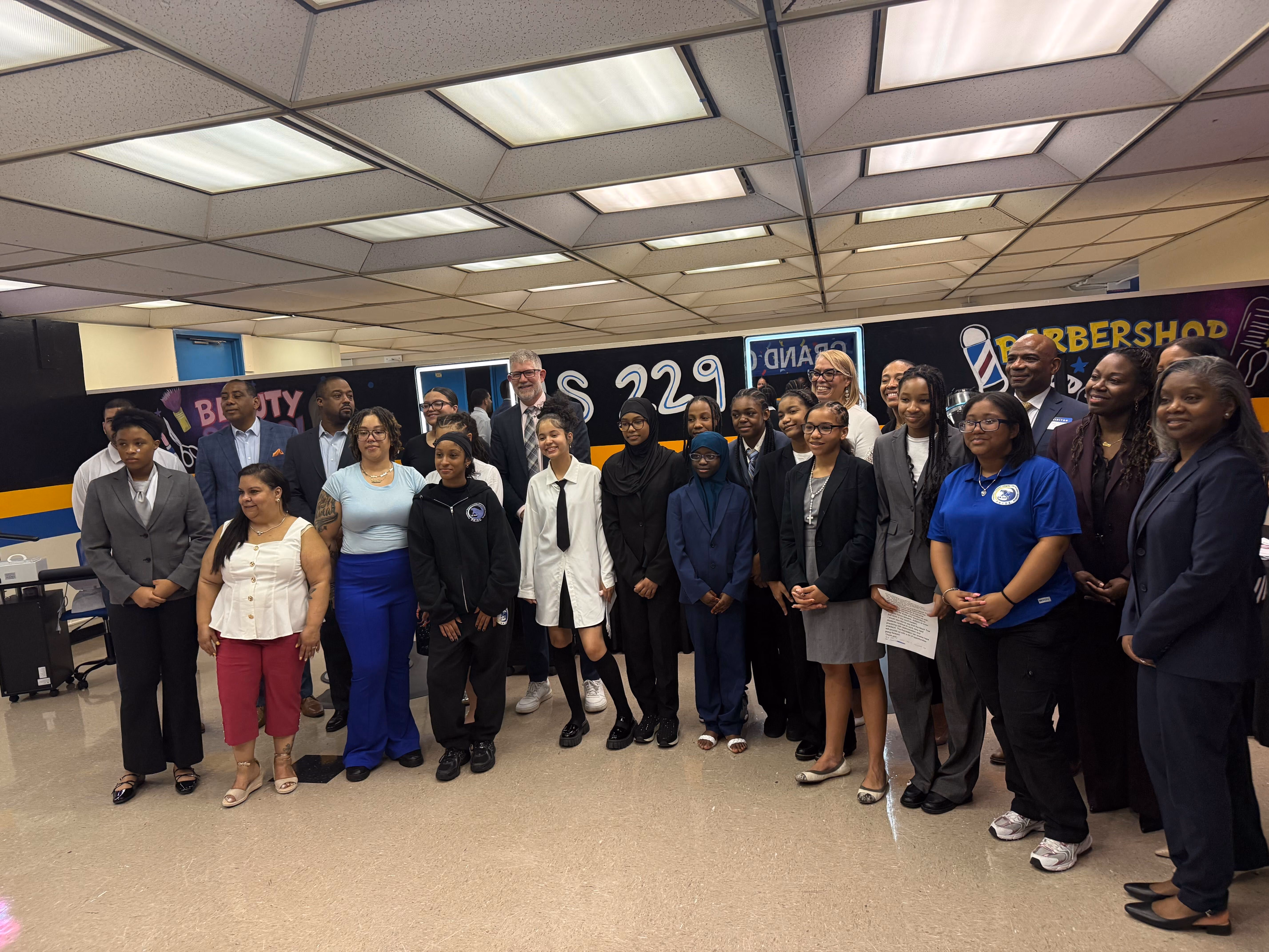 Students and staff pose together in IS 229 beauty and barbershop classroom