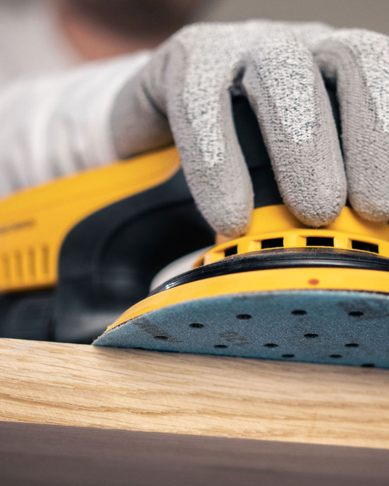 A hand held sander sanding a piece of wood