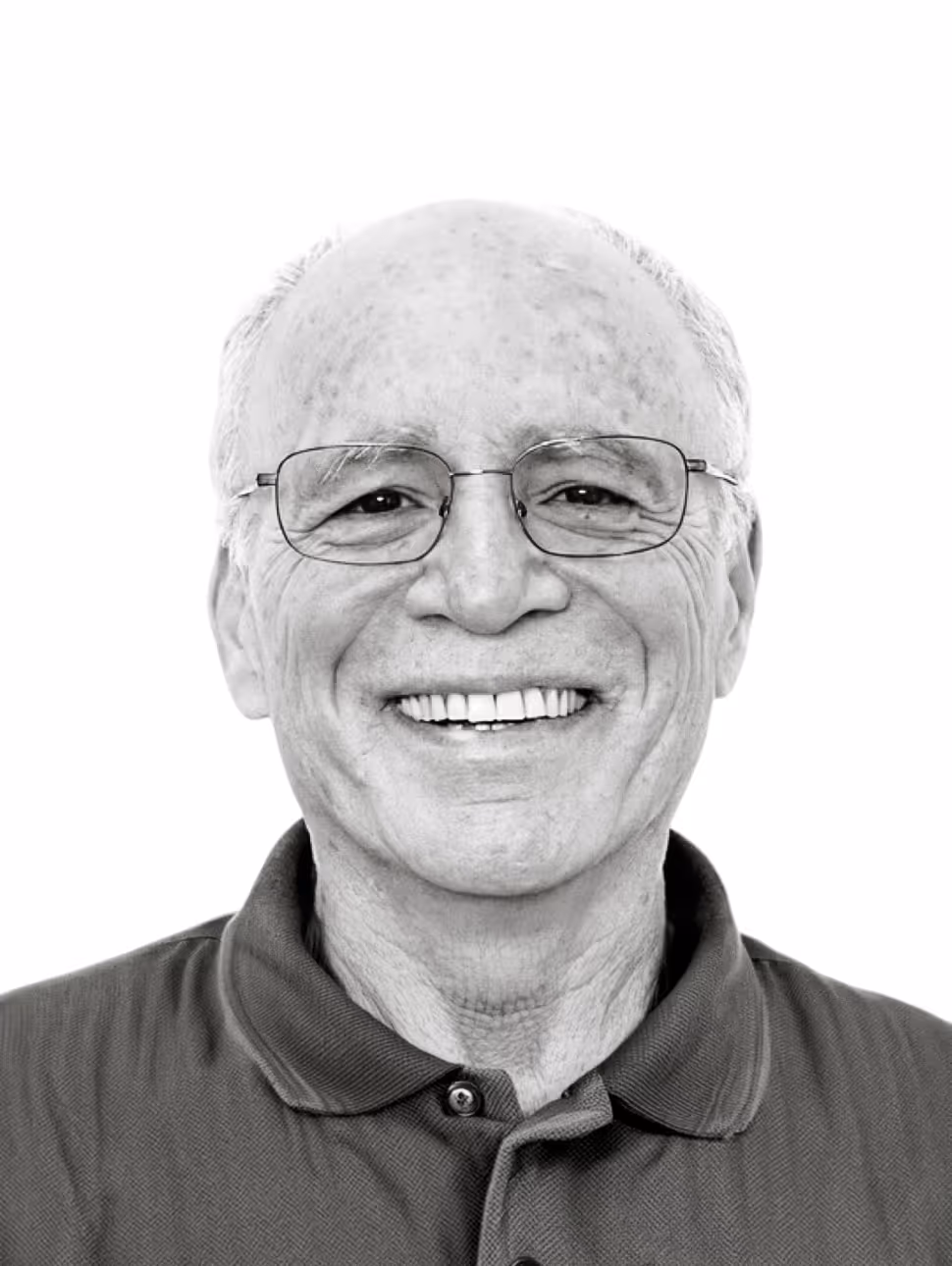 Smiling elderly man with glasses wearing a collared shirt against a white background.