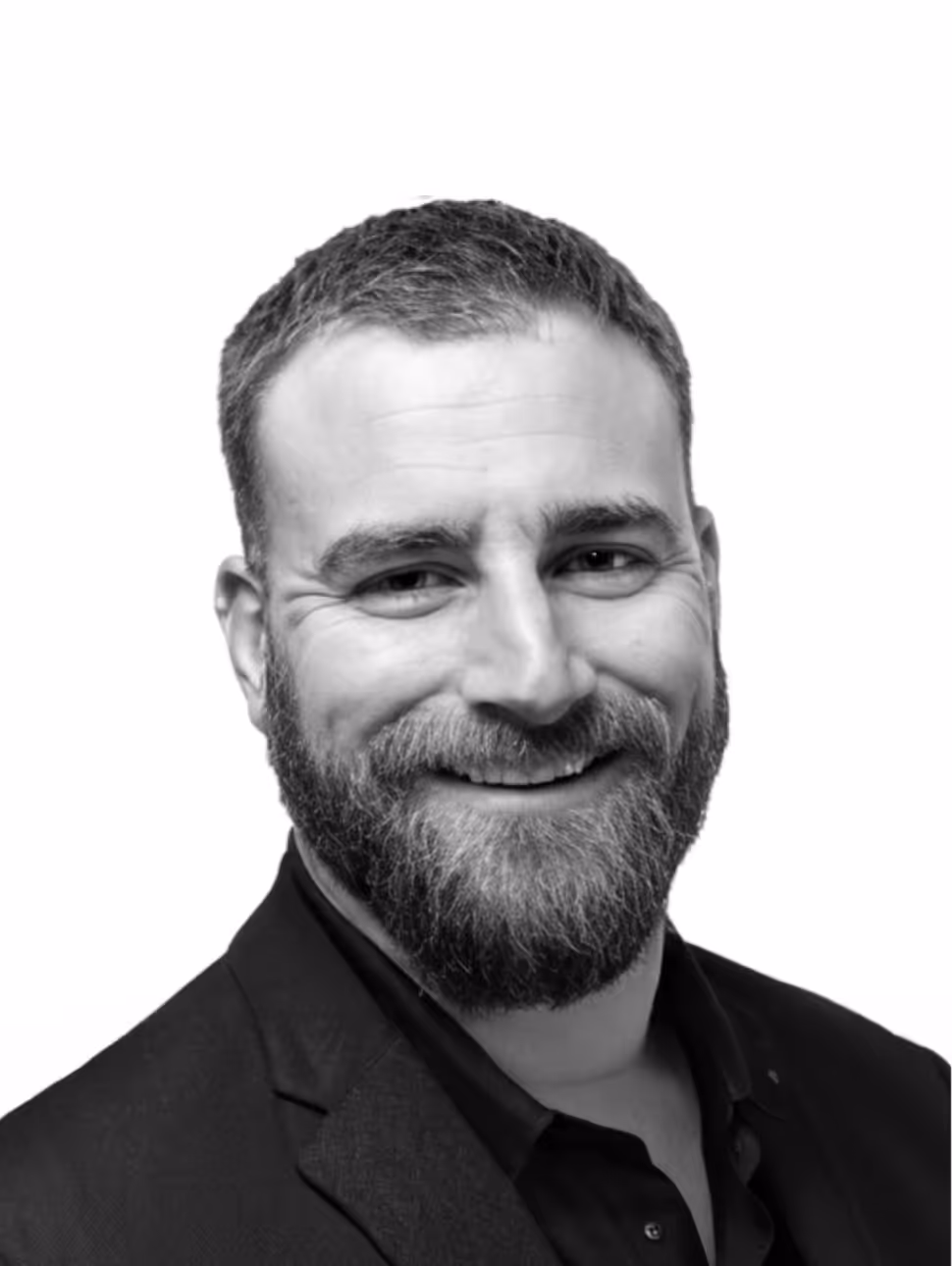 Smiling man with short hair and beard wearing a dark blazer and shirt on white background.