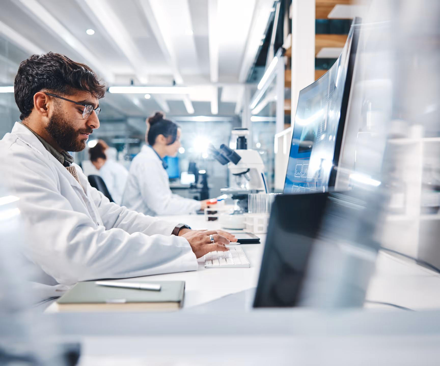 A lab researcher in a white coat working on a computer in a modern laboratory.