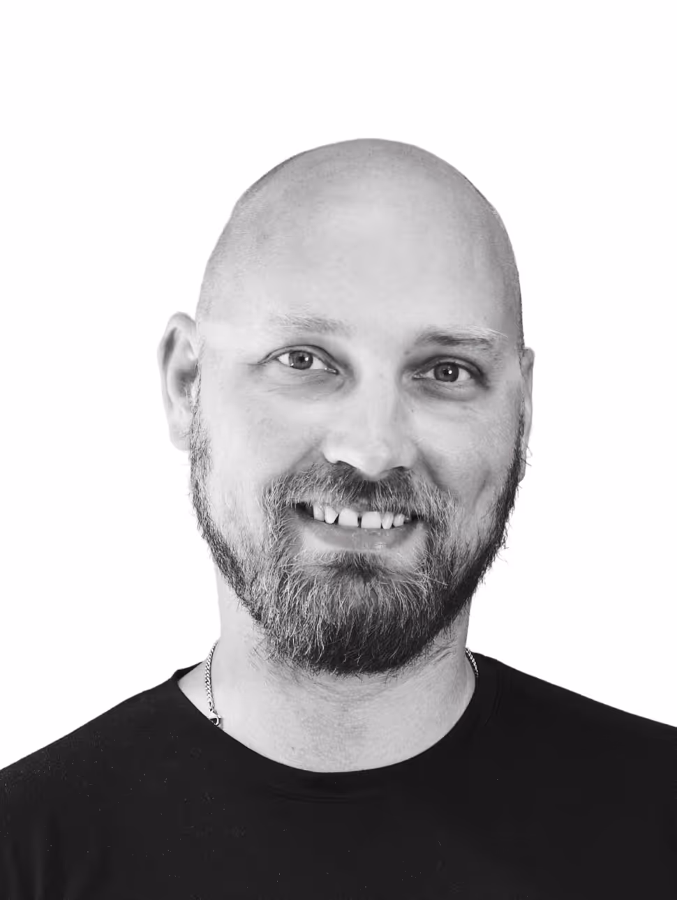 Smiling bald man with a beard wearing a black shirt and silver chain, head and shoulders portrait.